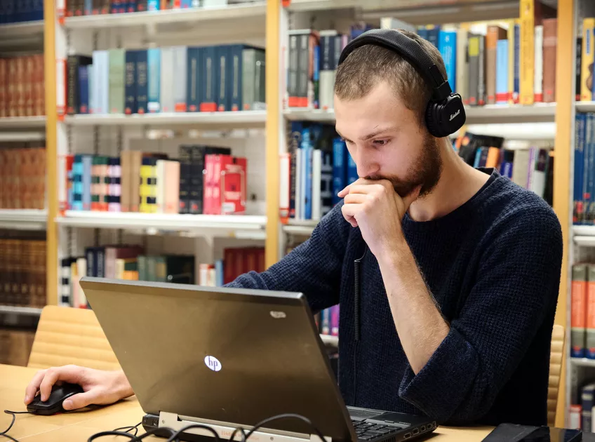 En man med hörlurar sitter vid en bärbar dator. Foto: Johan Bävman.